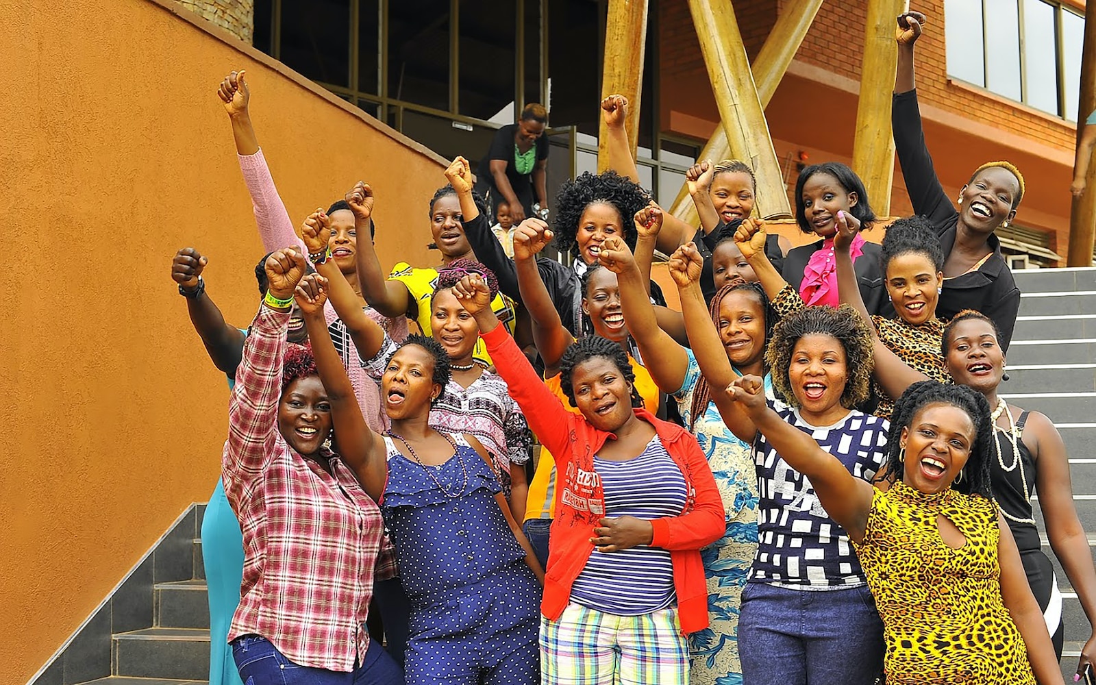 A group of smiling women stand on a stairway with arms raised