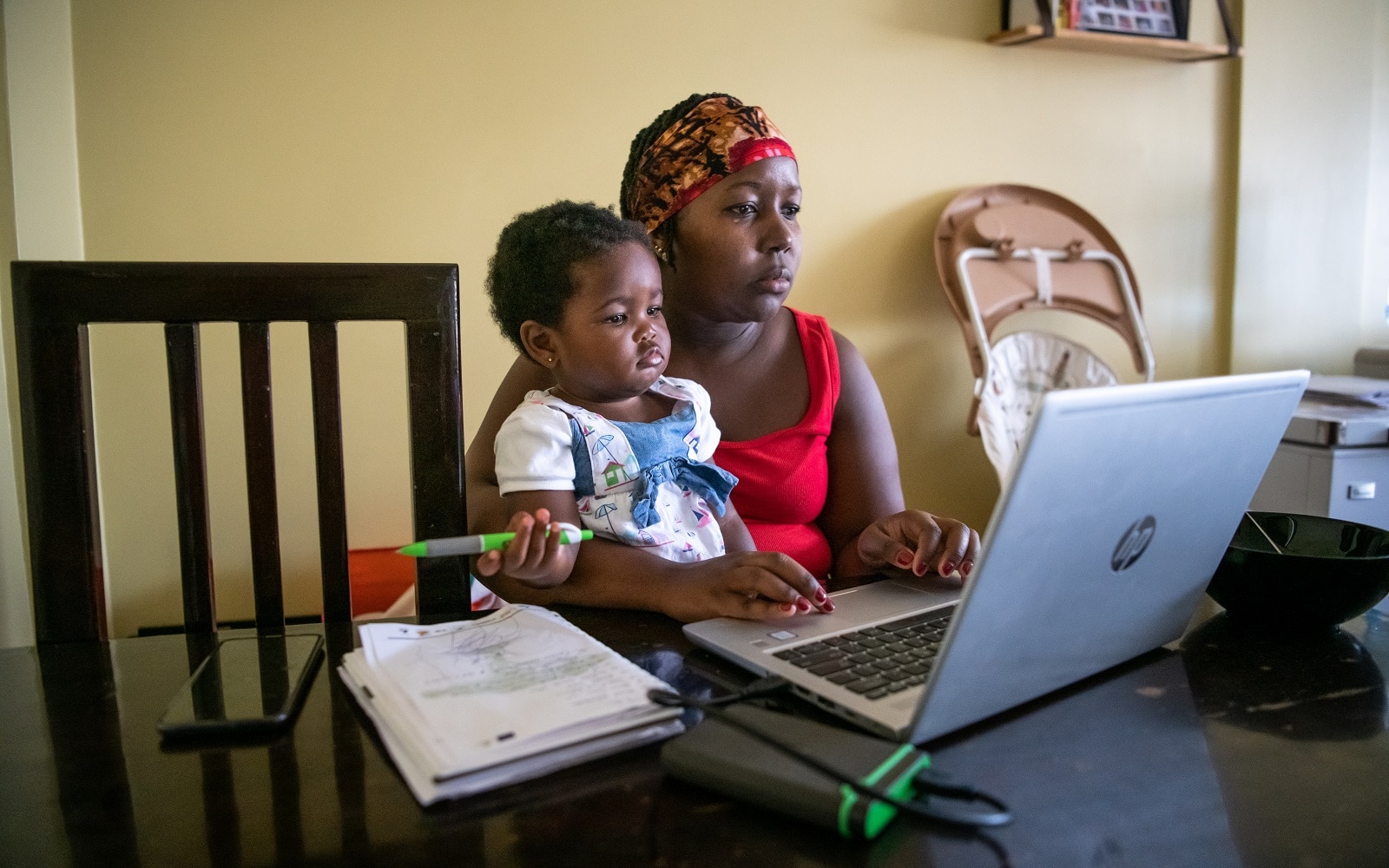 Woman working in front of laptop from home, with child on her lap.